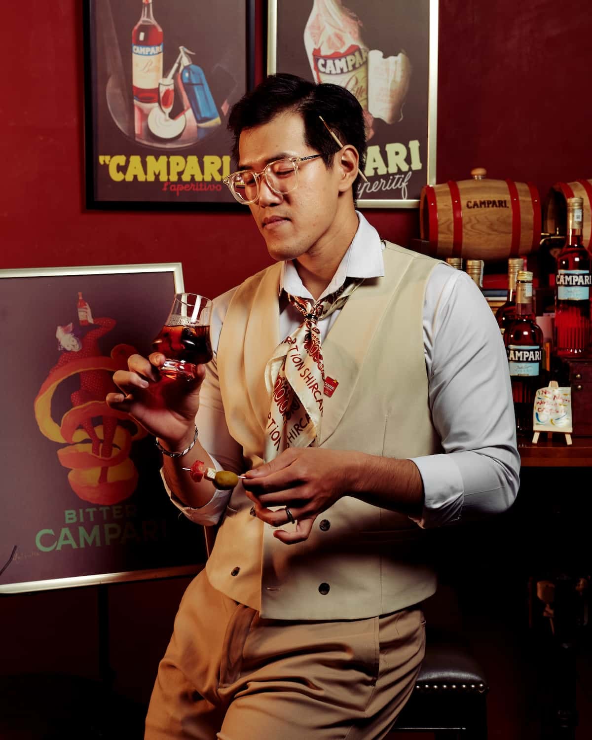 Bartender holding a red drink in front of Campari photos.