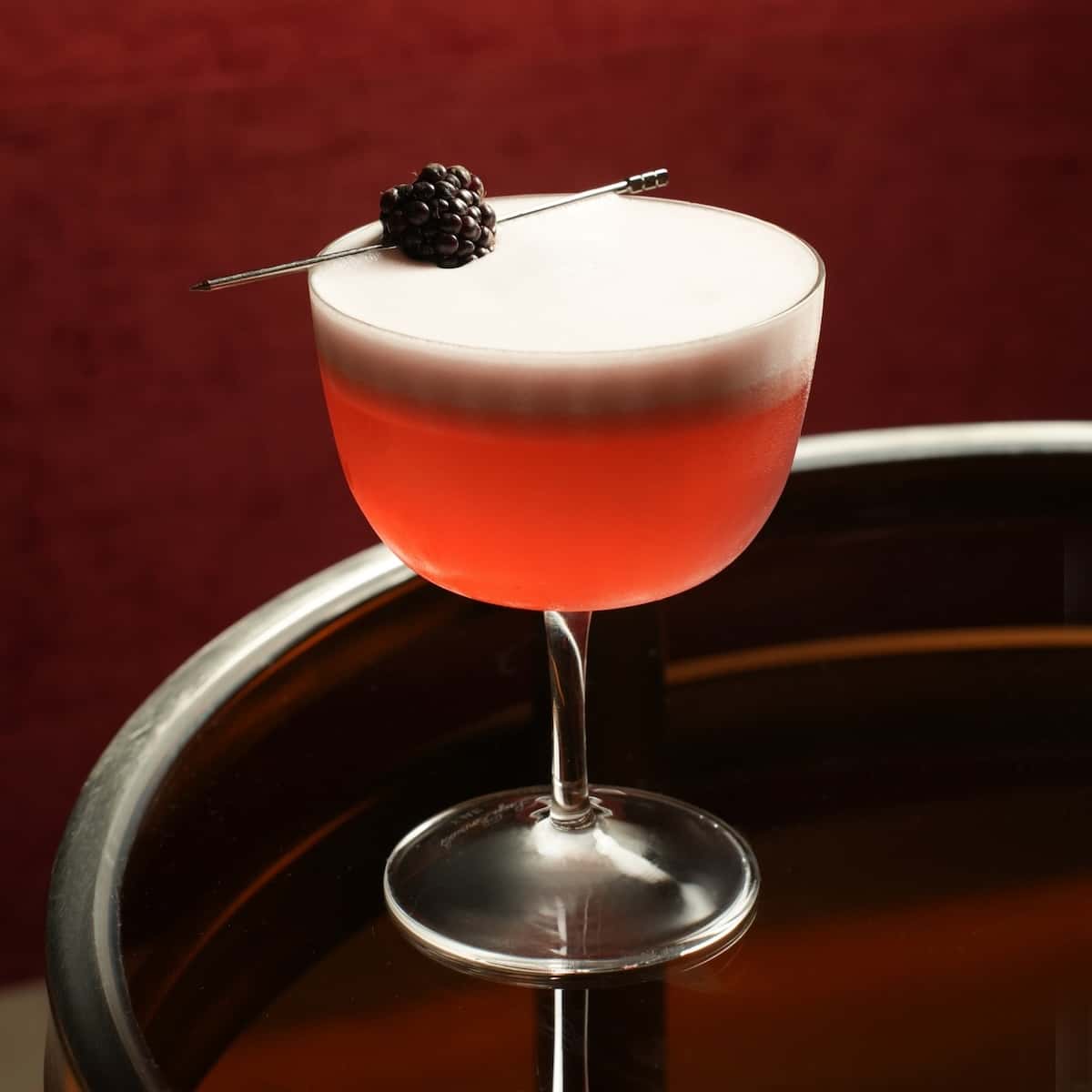 Berry on top of a red cocktail with a foam on top.