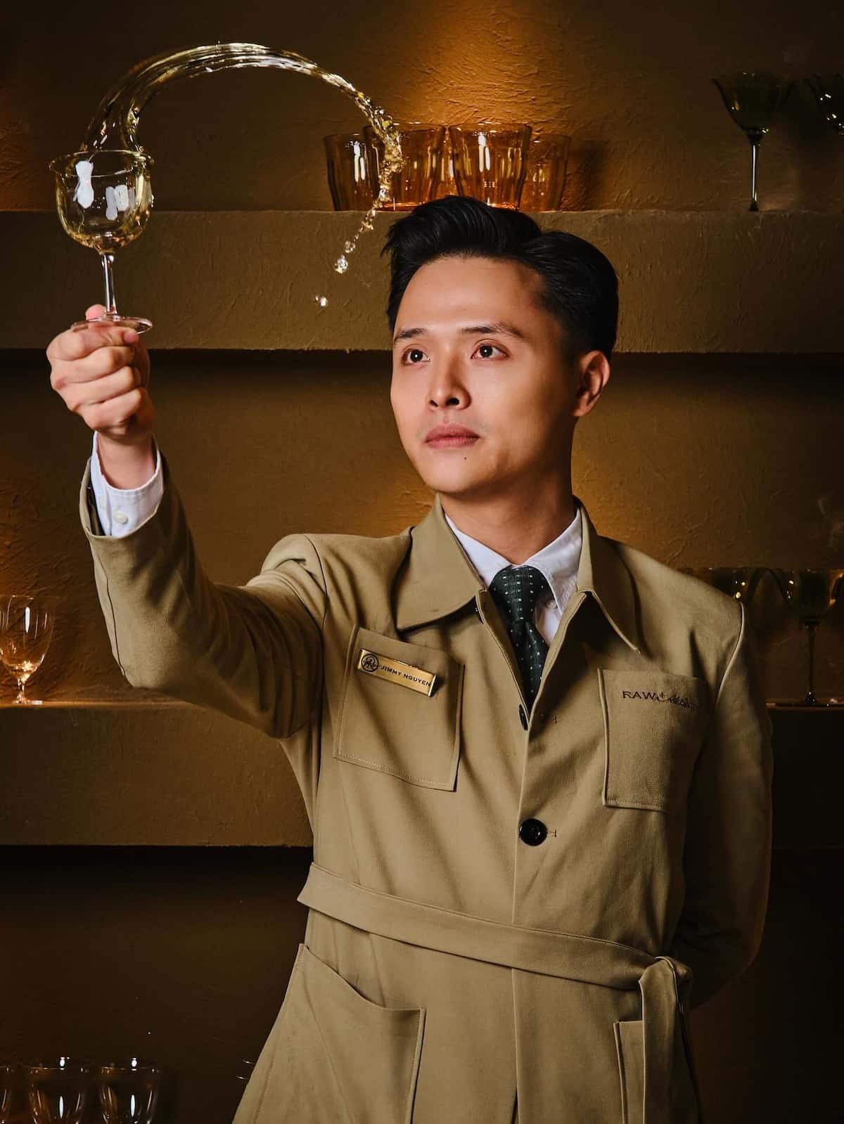 A bartender in a safari style jacket swirling a glass and the liquid is spiraling out.