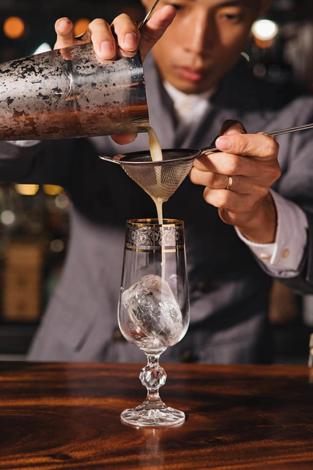 A bartender pouring a cocktail into a class.