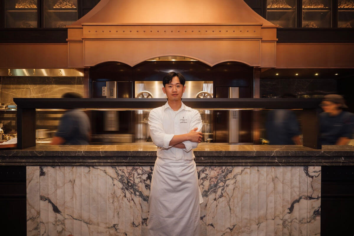 A chef in a kitchen in front of a fireplace hood.