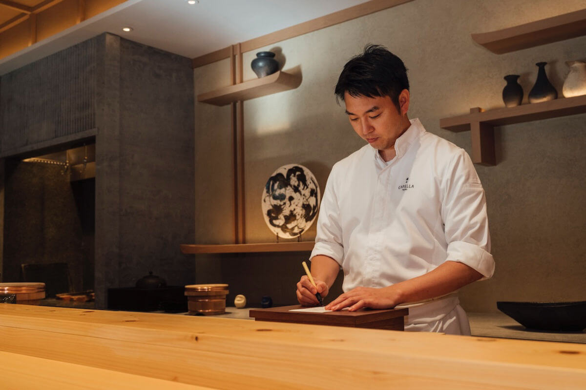 A chef in a white jacket behind a wooden counter.