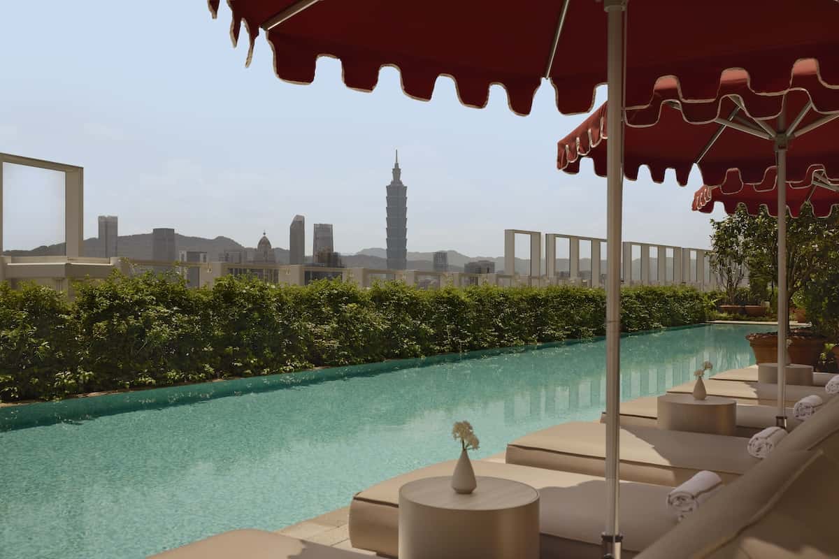 A pool and some loungers and in the distance a skyscraper.