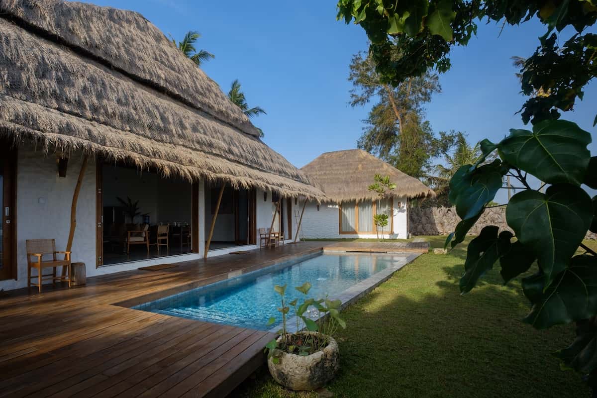 A beach house with a thatched roof and a pool outside.
