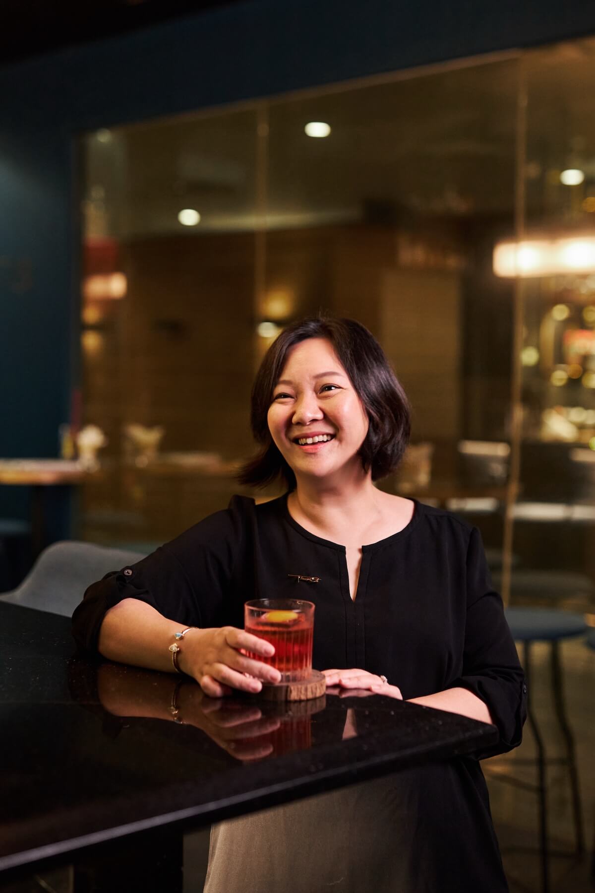 A smiling lady drinking a Negroni at the corner of a bar.