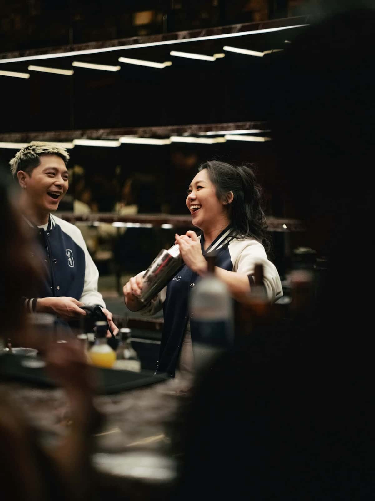 Two bartenders one shaking a cocktail.