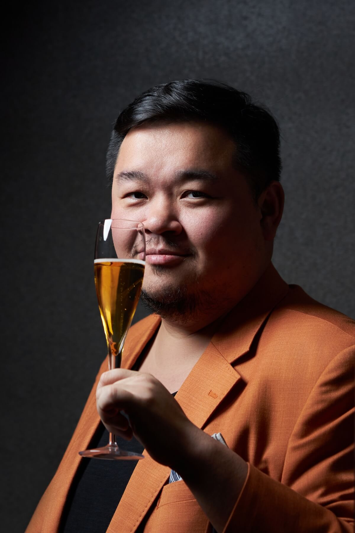 A man with a glass of sparkling wine and an orange jacket.