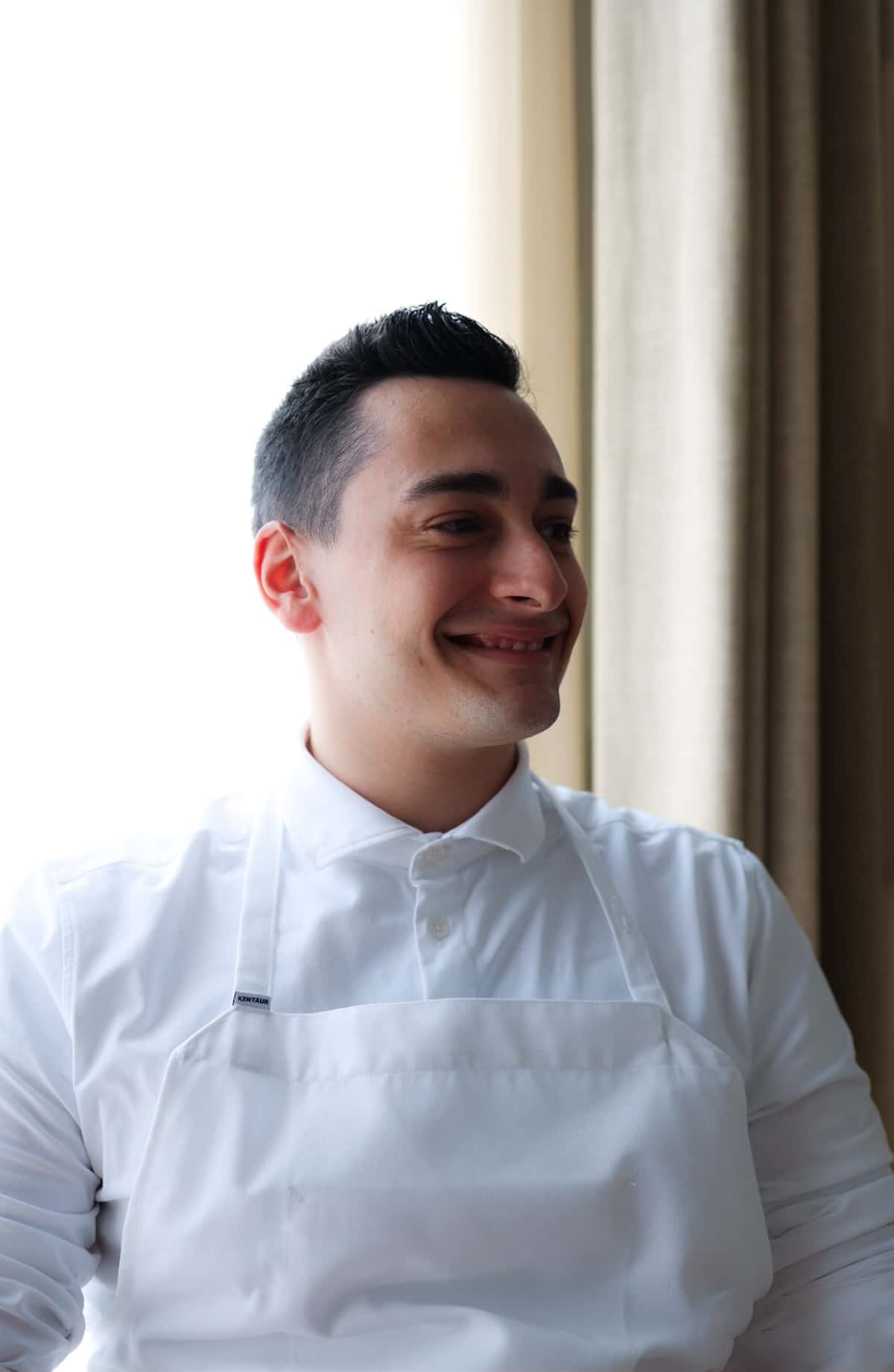 A man in a white apron smiling.