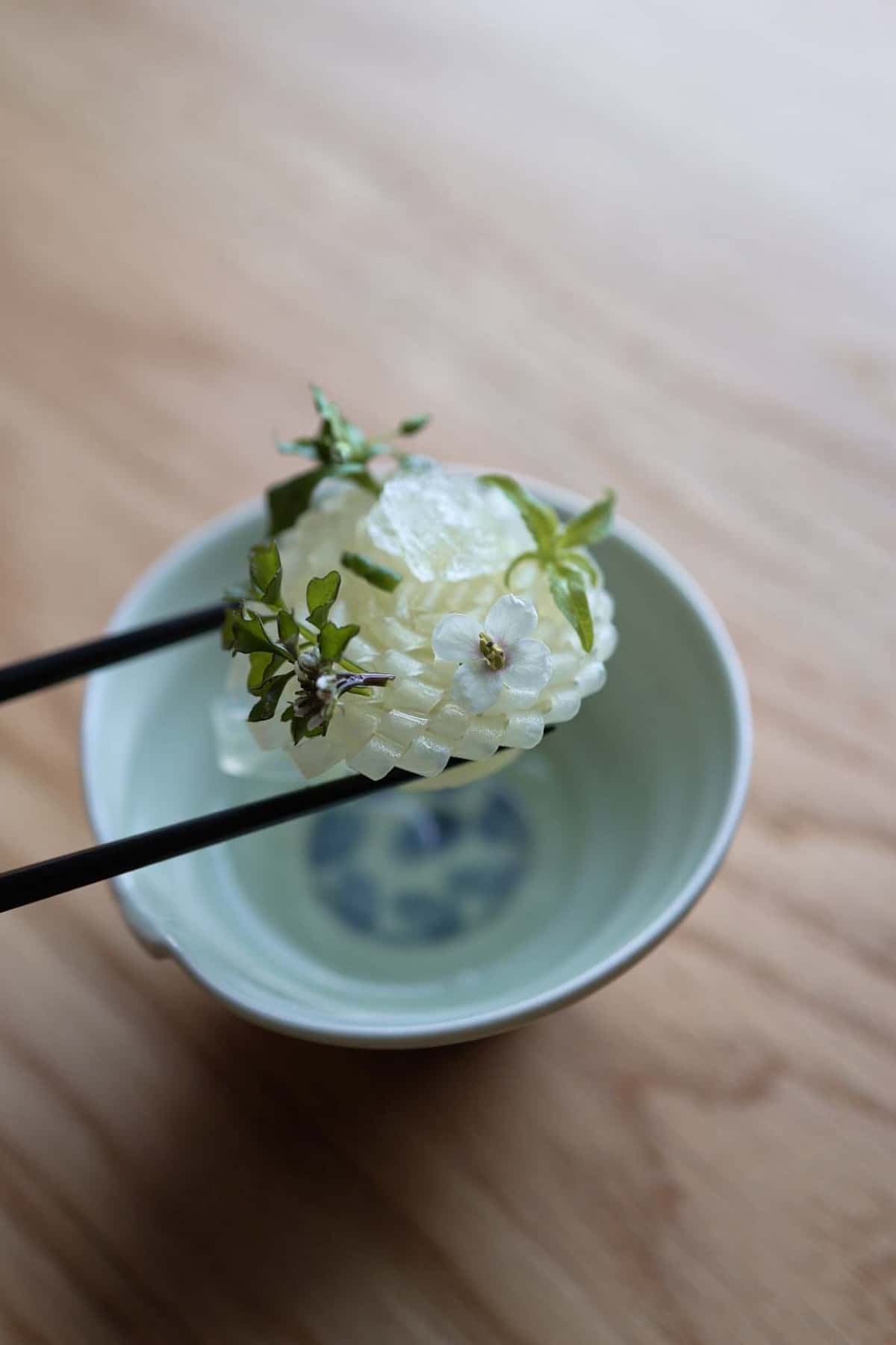 Chopsticks holding a white ball above a bowl.