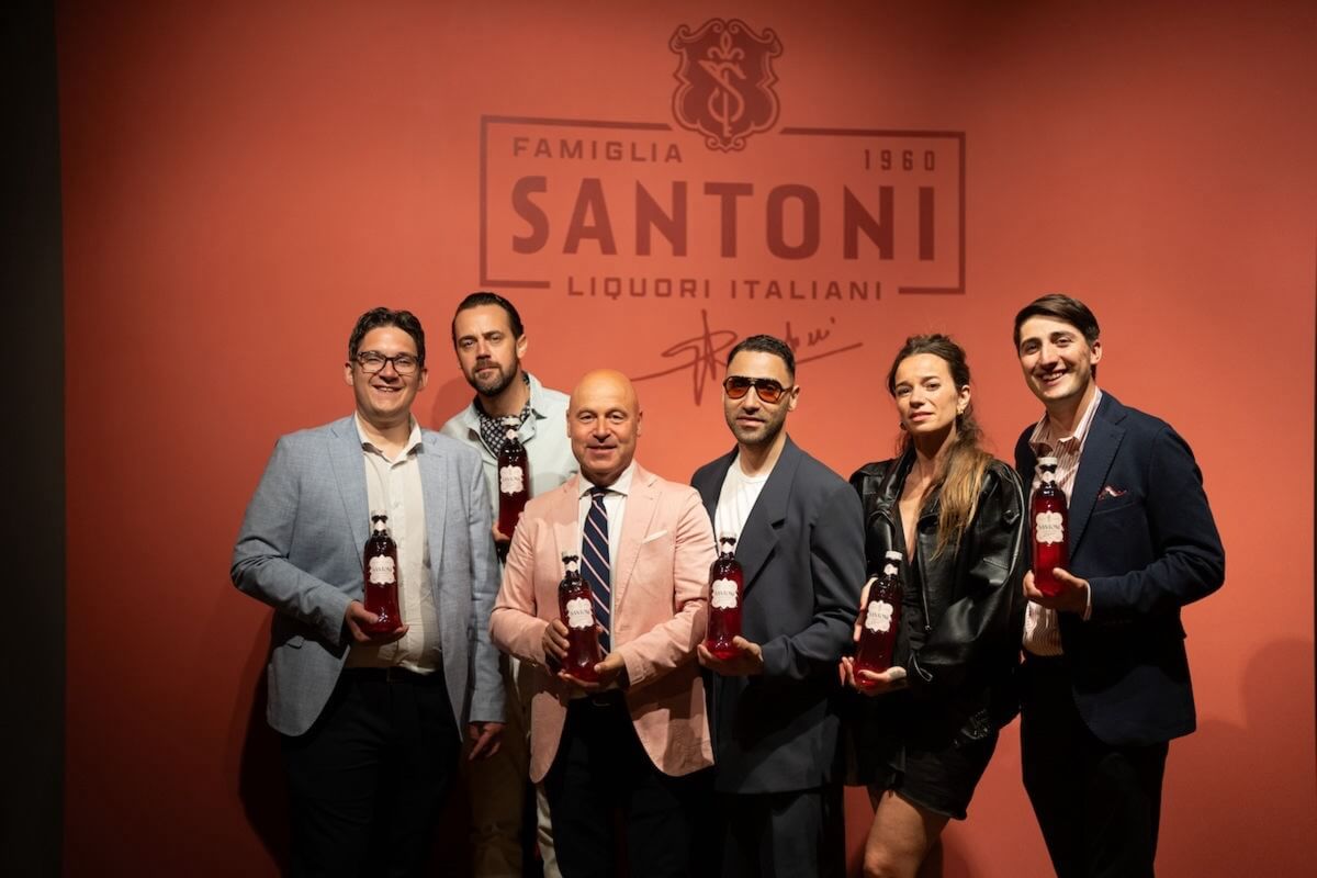 A group of people with red bottles in front of an orange wall.
