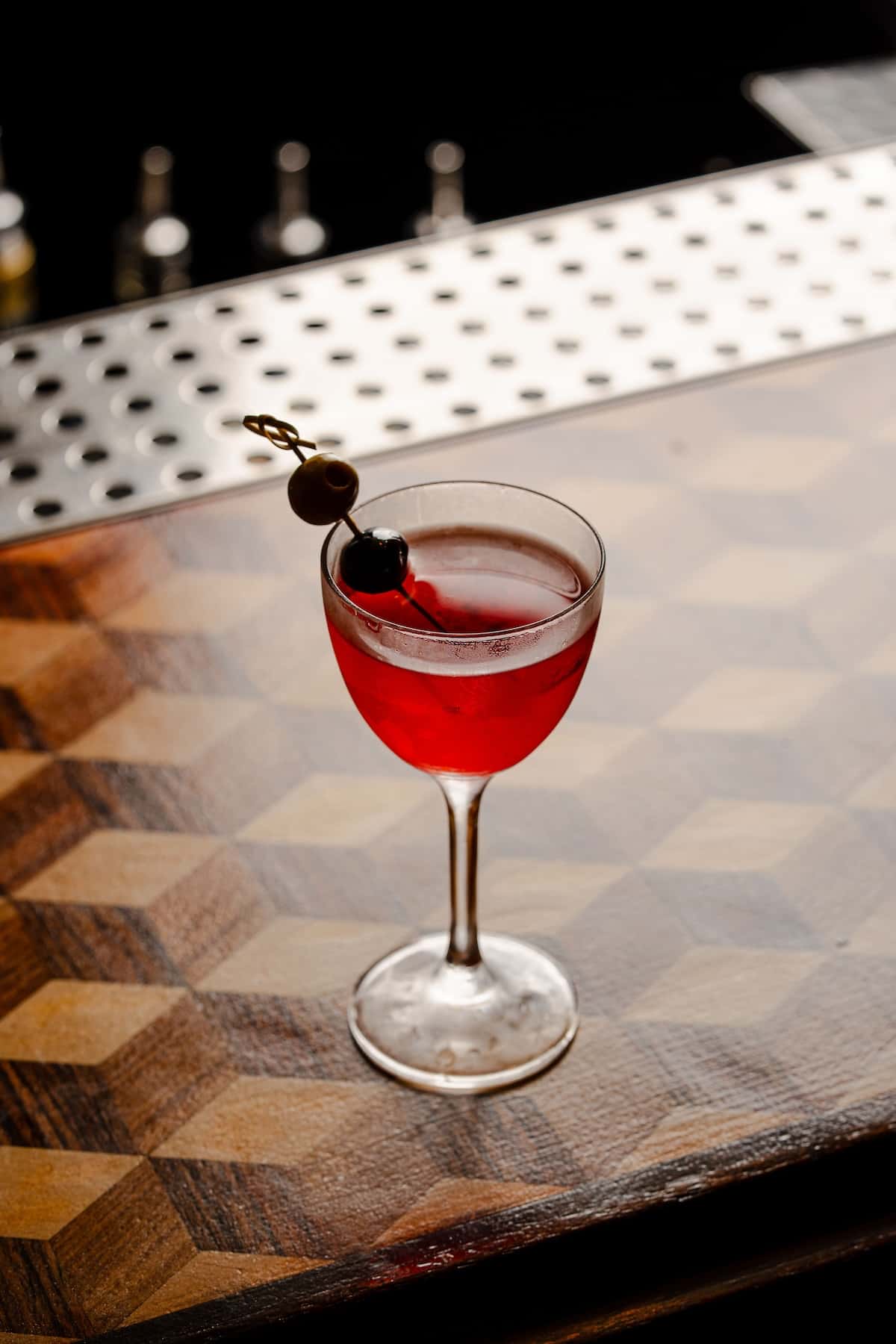 a glass of red liquid with a black olive on top